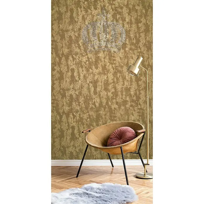 Glööckler Pompöös Provence Vliestapete Panel Krone - Gold, Metalloptik, 3 x 0,53 m - Einrichtungsszene mit einem stilvollen Sessel, einer Stehlampe und einem flauschigen Teppich vor einer goldenen Wand mit Kronenmuster.