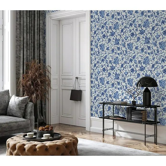 Glööckler Pompöös Provence Vliestapete - Grau/Blau, Floral, 10,05 x 0,53 m - Ein stilvolles Wohnzimmer mit einer Konsole mit einer Lampe und Büchern vor einer blau-weißen floralen Tapete.