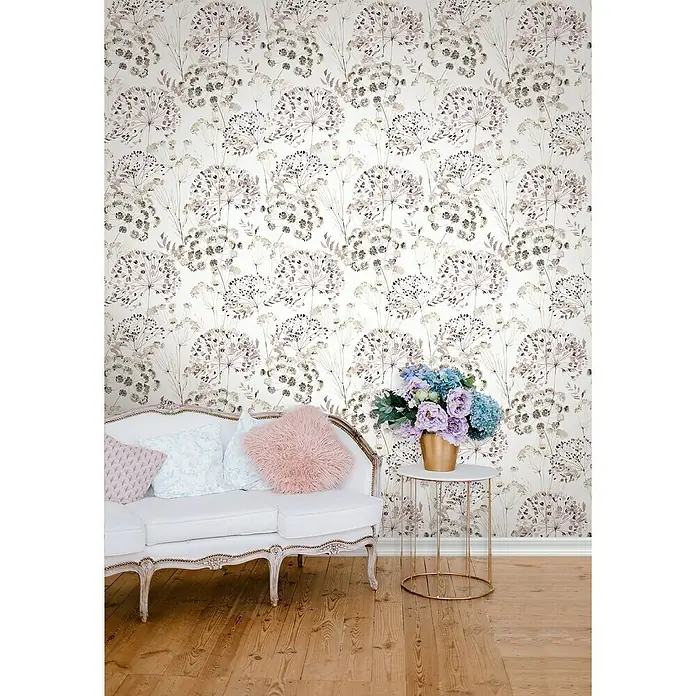 Glööckler Pompöös Provence Vliestapete - Grau/Beige/Rosa, Floral, 10,05 x 0,53 m - Elegantes Zimmer mit einer weißen Couch, Zierkissen und einem Beistelltisch mit Blumen vor einer floralen Tapete.