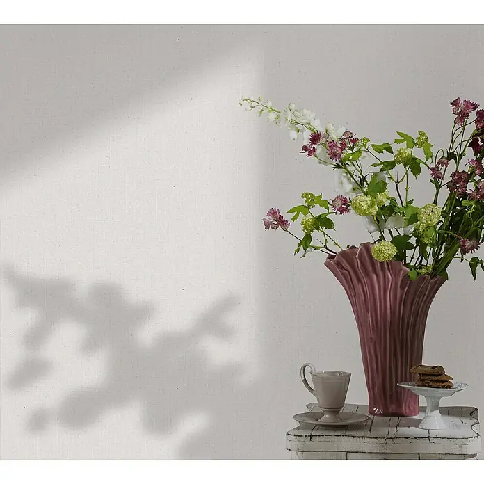 Glööckler Pompöös Provence Vliestapete - Offwhite, Uni, 10,05 x 0,53 m - Ein elegantes Stillleben mit einer hohen, geriffelten Vase, gefüllt mit üppigen Blumen, neben einer Teetasse und Keksen.