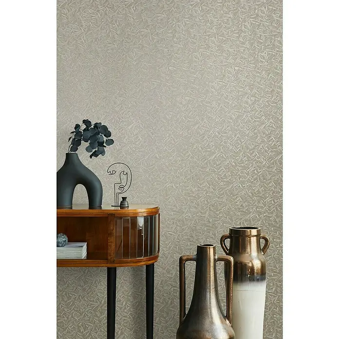 Glööckler Pompöös Provence Vliestapete Basic - Beige, Floral, 10,05 x 0,7 m - Nahaufnahme eines Raumes mit einem stilvollen Beistelltisch, einer Vase mit Blumen und dekorativen Objekten vor einer gemusterten Wand.
