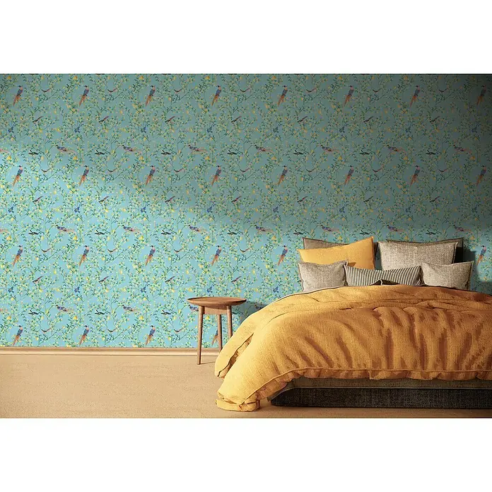 Glööckler Pompöös Provence Vliestapete - Blau/Grün/Gelb, Floral, 10,05 x 0,53 m - Gemütliches Schlafzimmer mit auffälliger Vogel-Tapete, senffarbener Tagesdecke und Nachttisch.