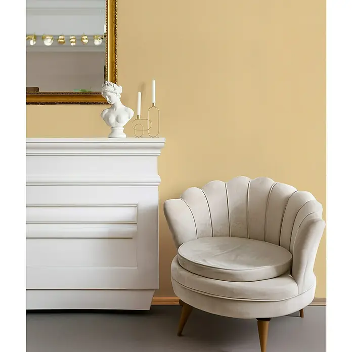 Glööckler Pompöös Provence Vliestapete - Gelb, Uni, 10,05 x 0,53 m - Stilvoller beiger Sessel mit Muscheldesign. Der Sessel steht neben einem weißen Kaminsims mit Spiegel und Büste für eine elegante Atmosphäre.