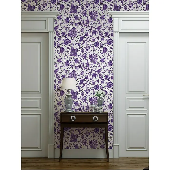 Glööckler Pompöös Provence Vliestapete - Grau/Lila, Floral, 10,05 x 0,53 m - Detailaufnahme eines Raumes mit einer Kommode mit Schublade, einer Lampe und Blumen vor einer lila gemusterten Tapete.