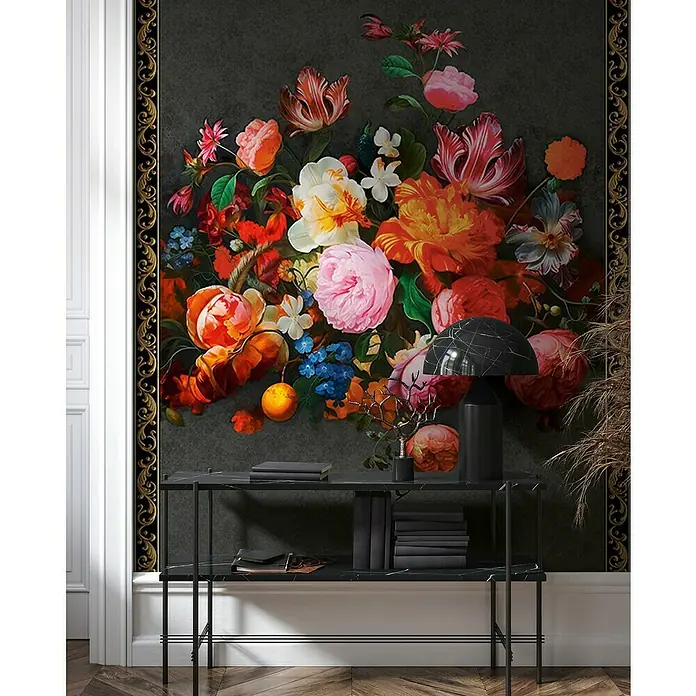 Glööckler Pompöös Provence Fototapete - Vlies, Schwarz/Rot - Wand mit opulentem Blumenmuster und filigranem Goldrahmen, darunter ein schlanker schwarzer Marmortisch mit Büchern und einer Lampe.