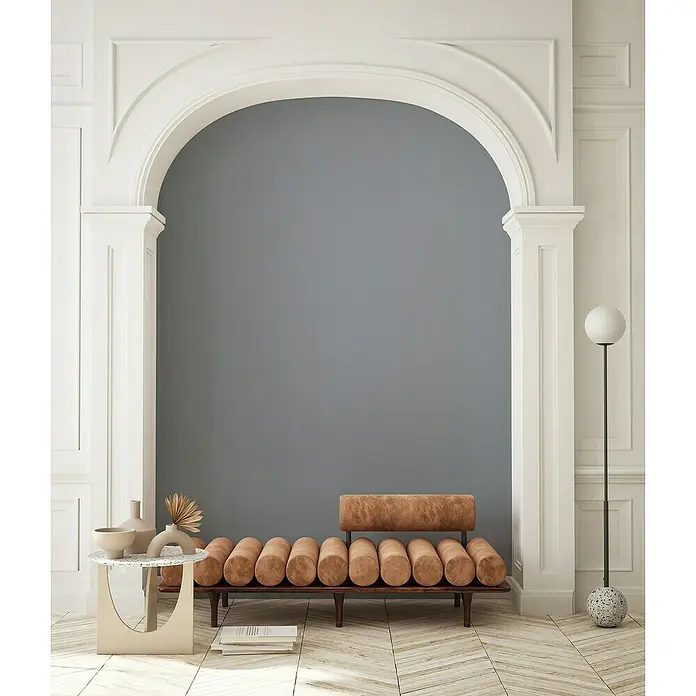 Glööckler Pompöös Provence Vliestapete - Mittelgrau, Uni, 10,05 x 0,53 m - Die Aufnahme zeigt ein stilvolles Tagesbett mit Rollenpolstern in einem eleganten Interieur mit architektonischem Bogen und Designelementen.