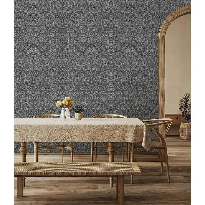Glööckler Pompöös Provence Vliestapete - Anthrazit/Schwarz, Ornament, 10,05 x 0,53 m - Ein Esstisch mit einer hellen Tischdecke, Blumen und einer Bank davor, beleuchtet durch das natürliche Licht in einem einladenden Raum.