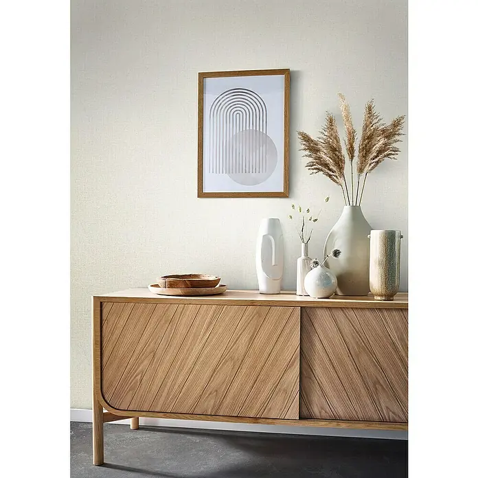 Glööckler Pompöös Provence Vliestapete - Greige, Uni, 10,05 x 0,53 m - Eine moderne Kommode aus Holz mit diagonalen Mustern auf den Türen und dekorativen Elementen darauf, die das Gesamtbild ergänzen.