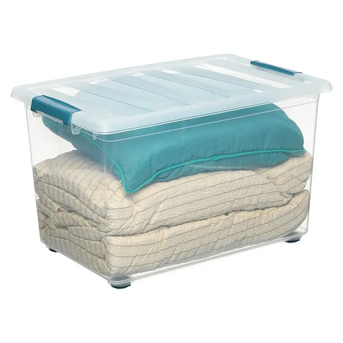 Caja con ruedas Katla - L x An x Al: 39 x 59 x 36,5 cm, 57 l - Un contenedor de almacenamiento de plástico transparente con tapa, lleno de una manta doblada y una almohada.