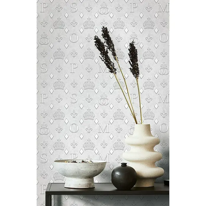 Glööckler Pompöös Provence Vliestapete - Grau, Grafisch, 10,05 x 0,53 m - Elegantes Interieur mit stilvoller Dekoration: Keramikvase, Schale und dunkle Kugel auf einem schwarzen Tisch vor gemusterter Tapete.