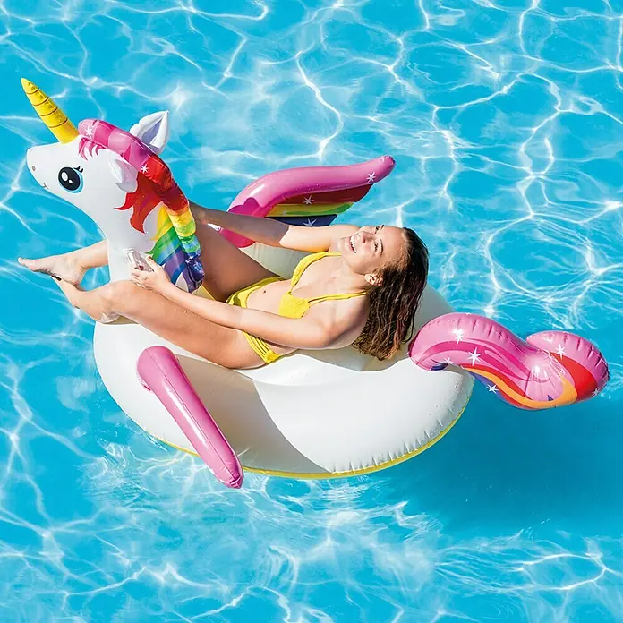 Intex Animal acuático Unicornio Isla L - 201 x 140 x 97 cm, Plástico, Multicolor - Una joven se relaja sobre un flotador inflable de unicornio en una piscina, disfrutando del sol. El unicornio es blanco con detalles arcoíris y rosas.