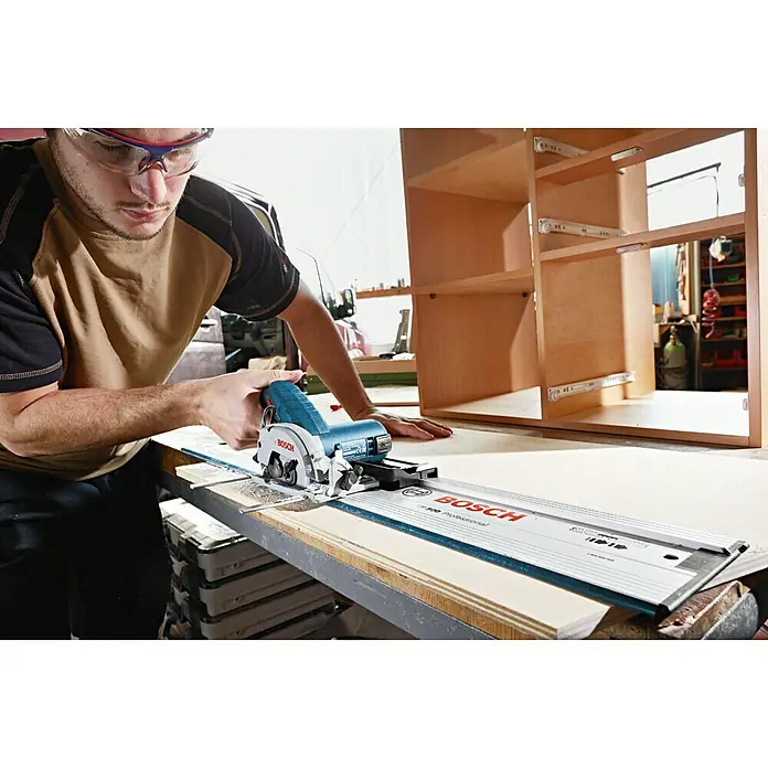 Bosch Professional Akku-Handkreissäge GKS 12V-26 L-Boxx - 12 V, Ohne Akku, Sägeblatt: 85 mm, Leerlaufdrehzahl: 1.400 U/min - Ein Mann benutzt eine Bosch Tauchsäge auf einer Werkbank mit einem unfertigen Holzschrank im Hintergrund.