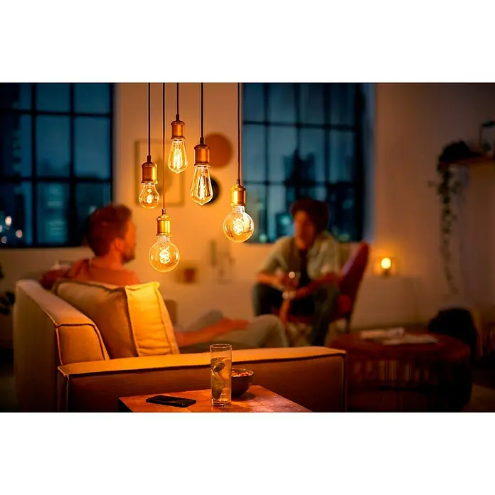 Philips Bombilla LED Vintage Gold - E27, No regulable, Ámbar, 300 lm, 5,5 W, Globo - Esta imagen muestra una moderna lámpara colgante con bombillas de luz blanca cálida, creando un ambiente acogedor en una sala de estar elegante.