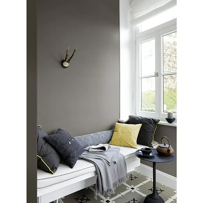 Alpina Wandfarbe Feine Farben - Stärke der Berge, Matt, 2,5 l, Konservierungsmittelfrei - Gemütliche Leseecke mit grauer Wand, Geweih, Fensterplatz mit Kissen, Decke und kleinem Tisch mit Teekanne, ideal zum Entspannen.