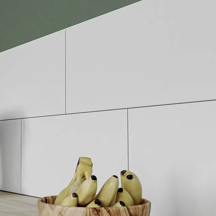 Ambiente by Palazzo Wandfliese Snowwhite New - 30 x 60 cm, Stärke: 9 mm, Weiß, Matt - Eine Nahaufnahme einer Schale mit Bananen vor einer weißen Wand mit einem grünen Streifen an der Oberseite.