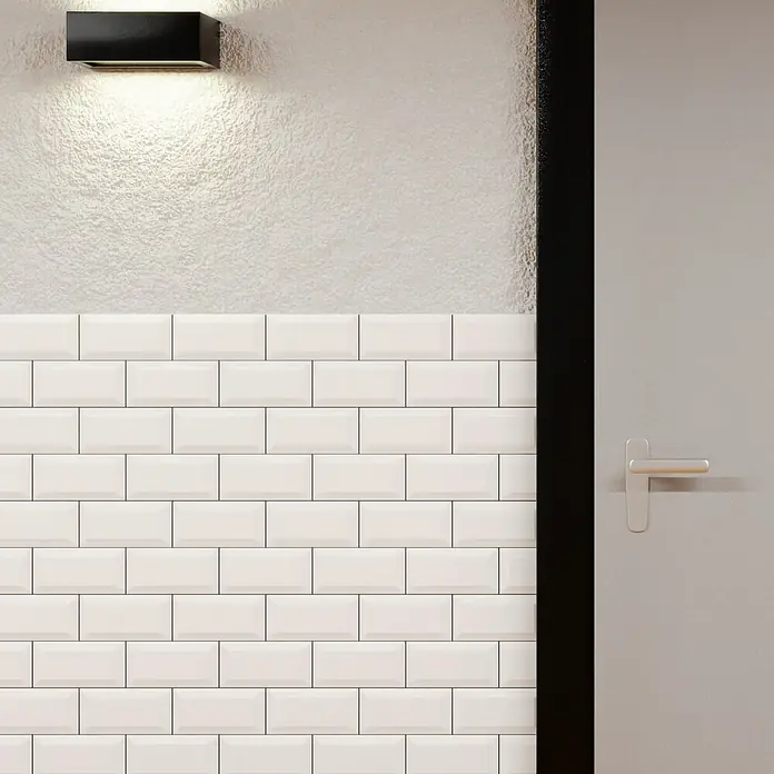 Modern Style Wandfliese Manhattan Biselado Blanco - 7,5 x 15 cm, Weiß, Matt - Wandleuchte mit einer rechteckigen Form, die ein sanftes Licht auf eine strukturierte Wand wirft, über einer weißen Fliesenfassade.