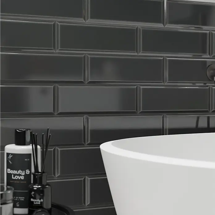 Modern Style Wandfliese Manhattan Biselado Cince 670 - 9,8 x 29,8 cm, Anthrazit, Glänzend - Nahaufnahme von "Beauty & Love"-Produkten auf einem schwarzen Tablett vor glänzenden schwarzen Metrofliesen und einer weißen Badewanne.