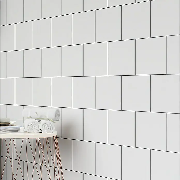 Wandfliese - 15 x 15 cm, Weiß, Matt - Detailaufnahme einer Badezimmerwand mit weißen Metrofliesen, die ein sauberes, modernes Design zeigen. Auf einem kleinen Tisch liegen gerollte Handtücher.