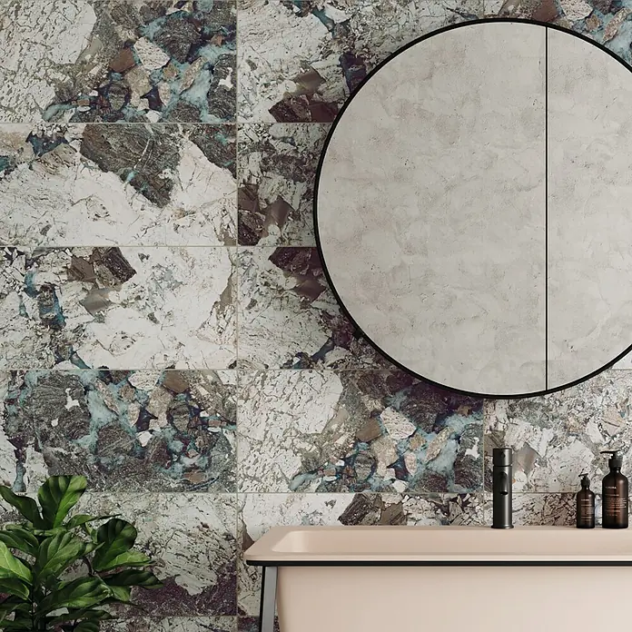 Domicil Wandfliese Stone Art Landscape - 30 x 60 cm, Blau/Grau/Beige, Glänzend - Ein Badezimmer mit Terrazzo-Fliesenwand und einem runden Spiegel. Die Fliesen sind ein echter Blickfang.