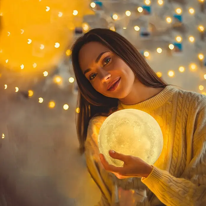 Voltomat Tischleuchte Luna - 15 W, Weiß, RGB - Frau hält eine leuchtende Mondlampe in ihren Händen, umgeben von warmem Licht.