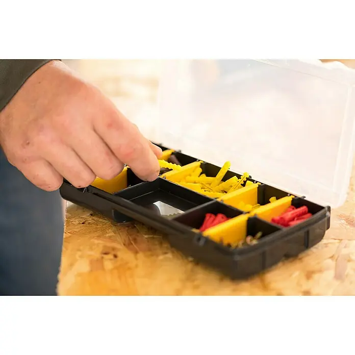 Stanley Kleinteilekoffer - Anzahl Fächer: 10 Stk., Ohne Inhalt, Schwarz/Gelb - Nahaufnahme einer schwarzen Sortierbox mit gelben und roten Dübeln, die von einer Hand durchsucht wird, ideal für Heimwerker und Werkstatt.