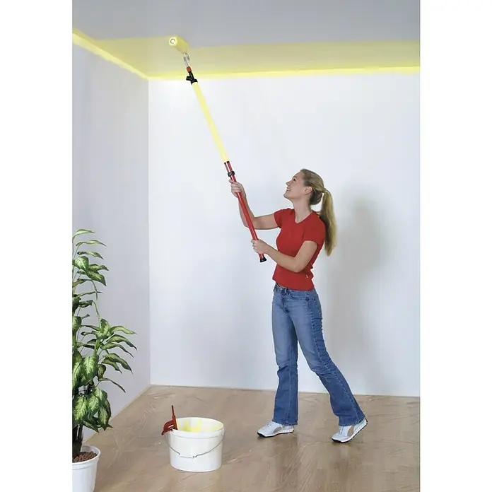 Lehnartz Farbroller Paint-Stick XXL - Breite Rolle: 230 mm, Längenverstellung: 950 mm - 1.500 mm - Eine Frau streicht mit einer gelben Farbrolle und einem roten Verlängerungsstab eine Decke. Die Zimmerdecke wird mit der Farbrolle gestrichen.