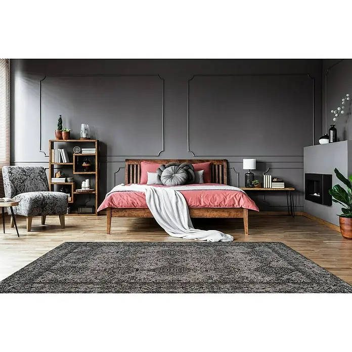 Kayoom Kurzflorteppich Iglesia - Grau/Schwarz, 290 x 200 cm, 100 % Polyester - Ein grauer Teppich mit detailreichem Muster liegt in einem Schlafzimmer mit Holzbett und grauen Wänden. Der Teppich verleiht dem Raum Atmosphäre.