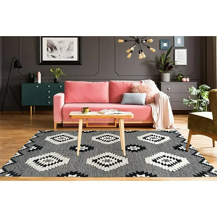 Kayoom Flachgewebeteppich Ethnie - Grau, 290 x 200 cm, 100 % Baumwolle - Ein Wohnzimmer mit einem gemusterten Teppich in Grau, Weiß und Schwarz, einem rosa Sofa und einem Holztisch.