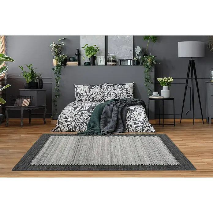 Kayoom Flachgewebeteppich Phoenix - Grau/Anthrazit, 170 x 120 cm, 75 % Wolle - Ein rechteckiger Teppich in Grau und Anthrazit liegt in einem Schlafzimmer mit Holzboden und passt perfekt zur Einrichtung.