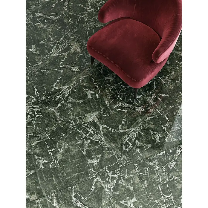 Atlas Concorde Solution Marble Vison Feinsteinzeugfliese Verde Bosco - 60 x 60 cm, Grün, Glänzend - Nahaufnahme eines Sessels aus bordeauxrotem Samt auf einem eleganten Boden aus grünen Marmorfliesen mit weißen Adern.