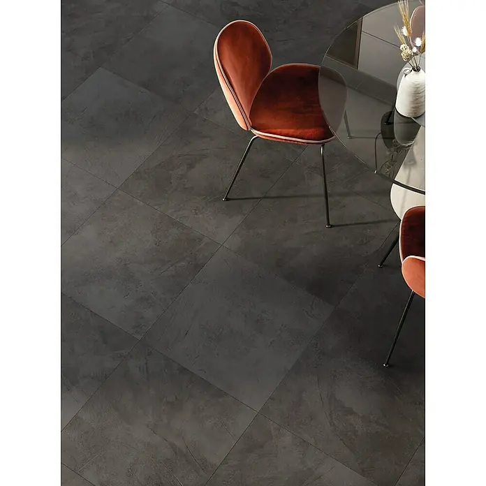 Atlas Concorde Solution Feinsteinzeugfliese Kaleidos Black - 60 x 60 cm, Schwarz, Matt - Dunkelgraue Bodenfliesen mit dezenter Textur in einem modernen Essbereich mit orangefarbenen Stühlen und Glastisch.