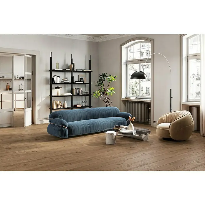 Atlas Concorde Solution Fable Feinsteinzeugfliese Cognac - 20 x 120 cm, Dunkelbraun, Matt - Ein Wohnzimmer mit einem stilvollen blauen Sofa, einem beigen Sessel und einem modernen Bücherregal, das einladend und komfortabel wirkt.