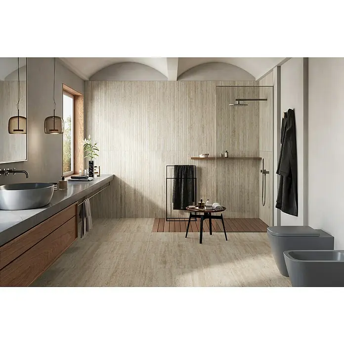 Atlas Concorde Solution Mosaikfliese Pompei Bianco Romano - Weiß, Matt - Modernes Bad mit beigen Steinfliesen, schwebendem Holzwaschtisch mit grauem Becken, begehbarer Dusche mit Holzlatten, grauer Wandtoilette und Bidet.