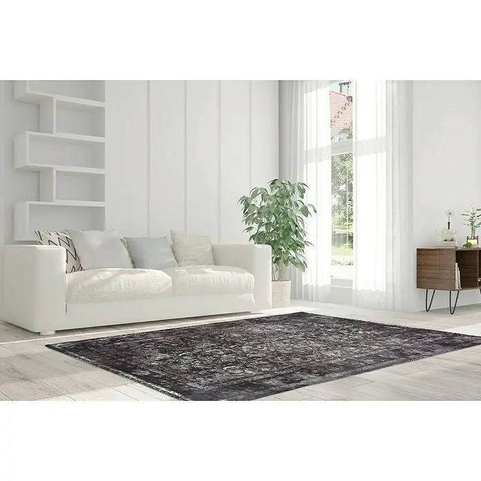 Kayoom Kurzflorteppich Vintage - Grau/Elfenbein, 200 x 140 cm, 100 % Polyacryl - Ein dunkler gemusterter Teppich liegt in einem hellen Wohnzimmer mit Sofa, Regal und Fenster.