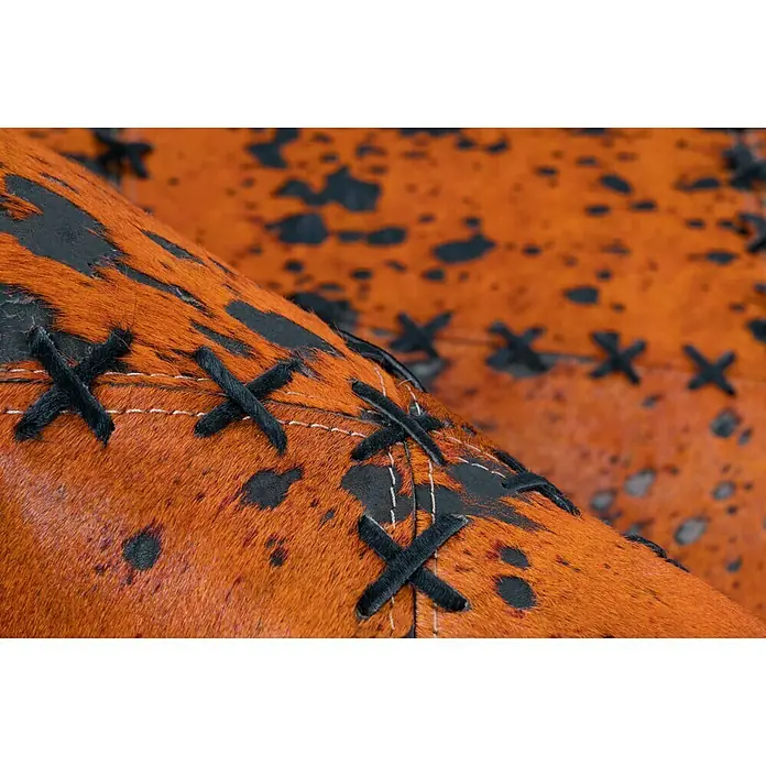 Kayoom Lederteppich Viola - Orange, 230 x 160 cm, 100 % Echtleder - Nahaufnahme eines braun-schwarz gefleckten Lederstuhls mit dekorativen, schwarzen Kreuzstichen. Detailreiche Verarbeitung für einen rustikalen Look.