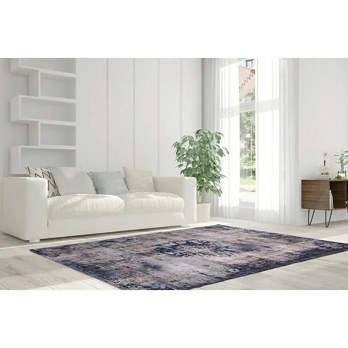 Kayoom Kurzflorteppich Vintage - Blau/Grau, 230 x 160 cm, 100 % Polyacryl - Ein grauer Teppich mit abstraktem Muster liegt in einem modernen Wohnzimmer mit weißem Sofa und hellen Holzböden. Der Teppich verleiht dem Raum einen Farbakzent.