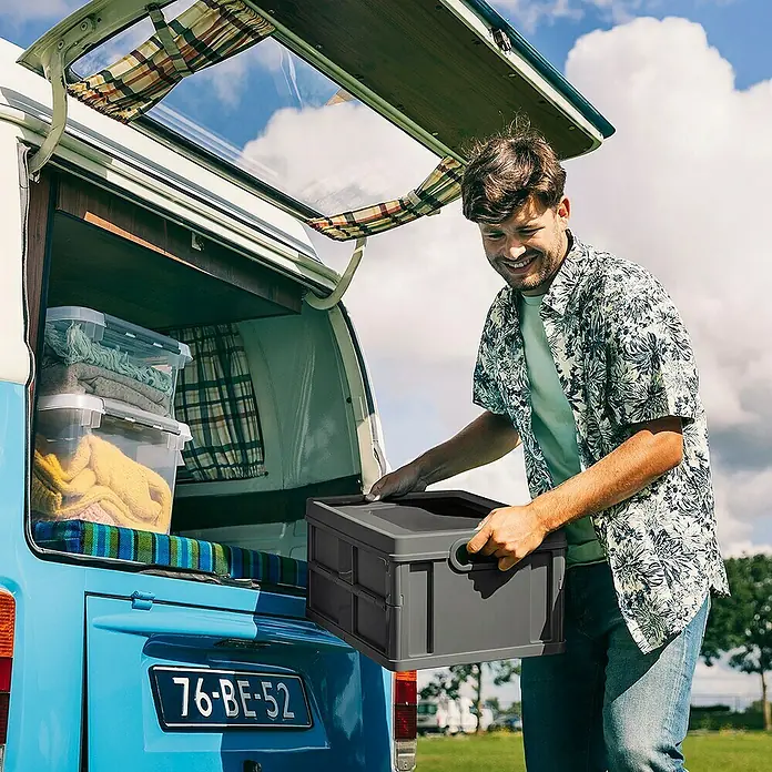 Sunware Klappbox Square - L x B x H: 49 x 36 x 24,5 cm, Anthrazit, Deckel - Ein Mann platziert eine dunkelgraue faltbare Kunststoff-Aufbewahrungsbox in einem blauen Wohnmobil zur Reiseaufbewahrung.