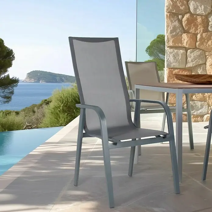 Bonlay Stapelsessel Nova - 4 Stk., Aluminium/Textilene, Anthrazit, B x T x H: 60 x 69 x 110 cm - Ein grauer Gartenstuhl aus Stoff und Aluminium steht neben einem Tisch und bietet einen Blick auf das Meer.