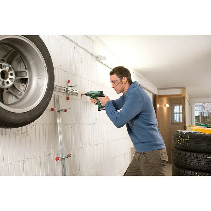 Bosch Power for All 18V Martillo perforador de batería Uneo Maxx - 18 V, Sin batería, 0,6 J - Un hombre usa un taladro inalámbrico Bosch para hacer agujeros en una pared para montar un estante para neumáticos.