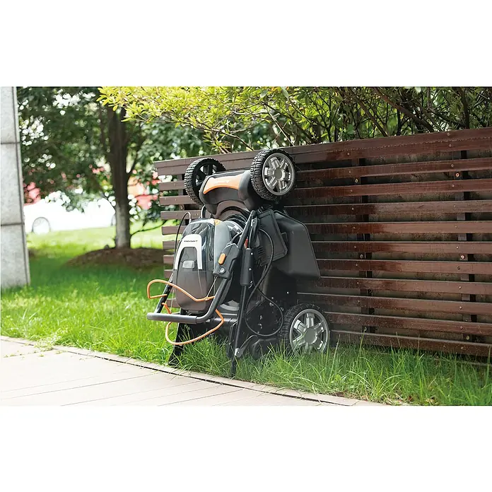 Yard Force Akku-Rasenmäher LM M46B - 60 V, 1 Akku, 4 Ah, Schnittbreite: 46 cm - Schwarzer und oranger Mähroboter steht aufrecht an einem Holzzaun im Garten.