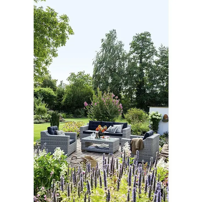 Sunfun Pauline Loungemöbel-Set XXL - 4 -tlg., Polyrattan, Bambusgrau/Anthrazit - Eine graue Rattansitzgruppe mit Sofa, Sesseln und Tisch im Garten, umgeben von üppiger Vegetation und bunten Blumen.