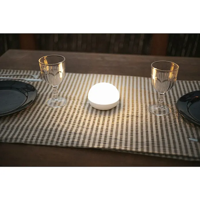 New Garden LED-Poolbeleuchtung Coco Floating Blulb - Durchmesser: 11 cm, Weiß, LED - Tischdekoration mit Gläsern und einer leuchtenden Kugel auf einem gestreiften Läufer.