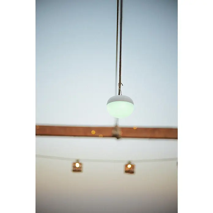 New Garden LED-Poolbeleuchtung Coco Floating Blulb - Durchmesser: 11 cm, Weiß, LED - Nahaufnahme einer hängenden, runden LED-Lampe mit einem weichen, grünen Licht, die an einer Schnur unter einer Holzstruktur befestigt ist.