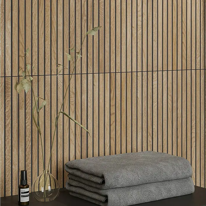 Wandfliese Boseli Wood - 29,8 x 59,8 cm, Beige, Matt - Nahaufnahme einer Wand mit Holzpaneelen, einem Stapel grauer Handtücher und dekorativen Elementen, die eine moderne Badezimmeratmosphäre schaffen.
