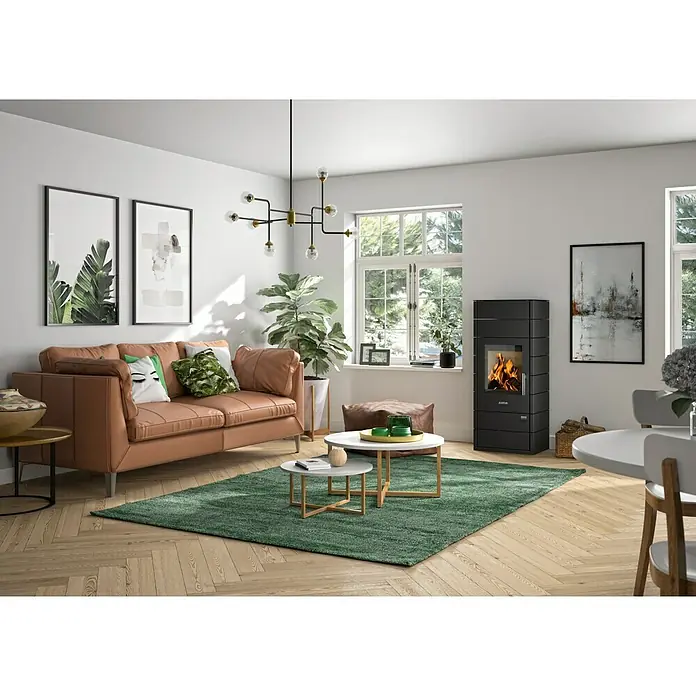 Justus Kaminofen Tova - 6 kW, Raumheizvermögen: 115 m³, Material Verkleidung: Stahl, Schwarz - Wohnzimmer mit schwarzem Justus Kaminofen, Sofa, Teppich und Dekorationen für ein gemütliches Ambiente mit Kaminfeuer.