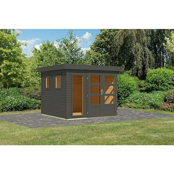 Karibu Gartenhaus Lahar - Außenmaß inkl. Dachüberstand (B x T): 266 x 262 cm, Holz, Terragrau, Ohne Seitendach - Ein modernes Gartenhaus in Anthrazit mit Flachdach und großen Fensterfronten. Das Häuschen steht auf einer gepflasterten Fläche inmitten eines Gartens.