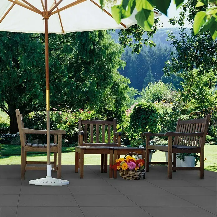 Terrassenplatte Wild Stone - 60 x 40 x 4 cm, Titanio, Beton - Einladende Gartenszene mit Terrassenfliesen und Sitzgruppe unter einem Sonnenschirm.