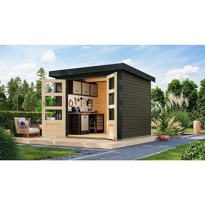 Karibu Gartenhaus Jupiter 3 B - Außenmaß inkl. Dachüberstand (B x T): 266 x 236,5 cm, Holz, Terragrau/Anthrazit - Geräumiges Gartenhaus mit Werkbank, Schränken und geöffneten Doppeltüren auf einer Holzterrasse, umgeben von üppigem Grün und einem gepflasterten Weg.