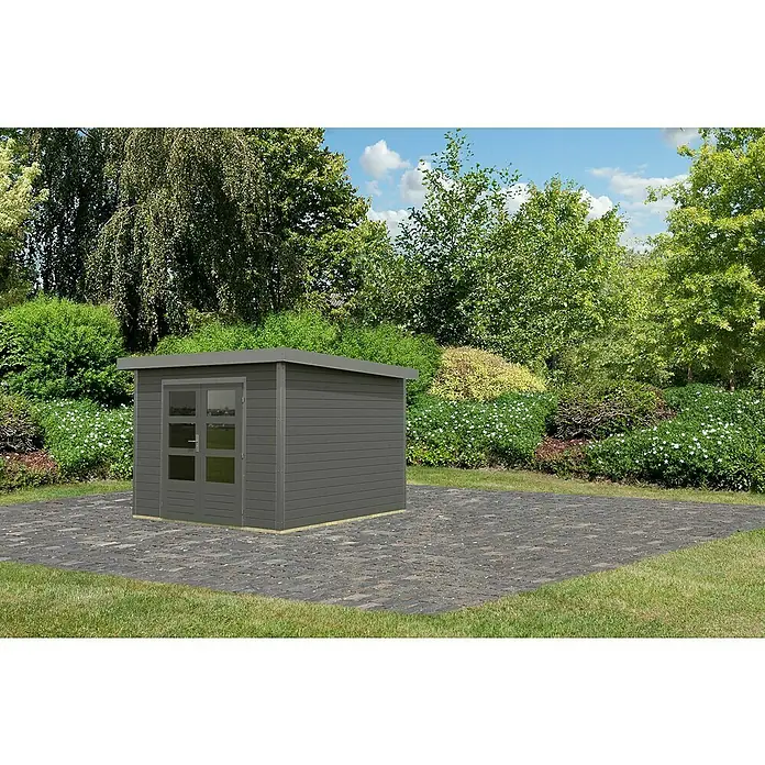 Karibu Gartenhaus Pluto 6 B - Außenmaß inkl. Dachüberstand (B x T): 309 x 292,4 cm, Holz, Terragrau/Grau - Ein graues Gartenhaus mit Doppeltür und Fenster steht auf einem gepflasterten Bereich, umgeben von Grünpflanzen und Bäumen.