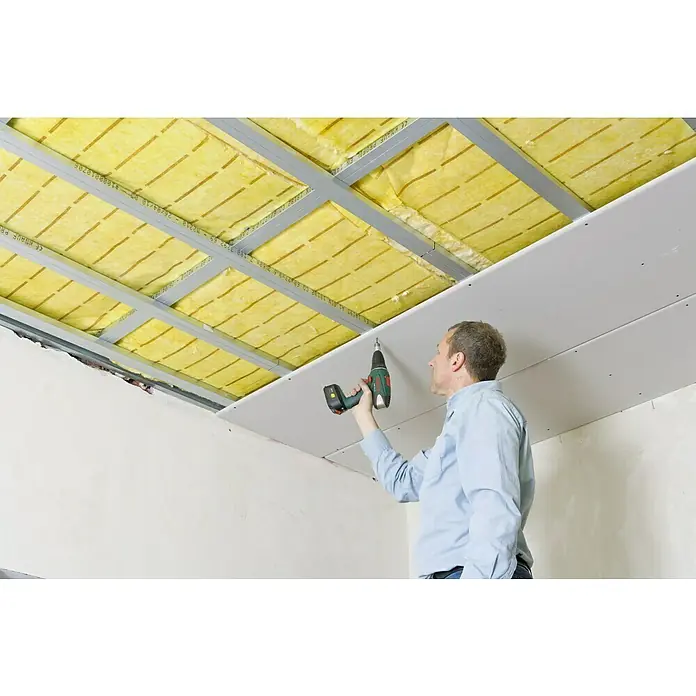 Knauf Gipskartonplatte Massiv GKF - 2.000 x 625 x 20 mm - Mann befestigt eine Gipskartonplatte mit einem Akkuschrauber an einer Deckenkonstruktion mit gelber Isolierung.